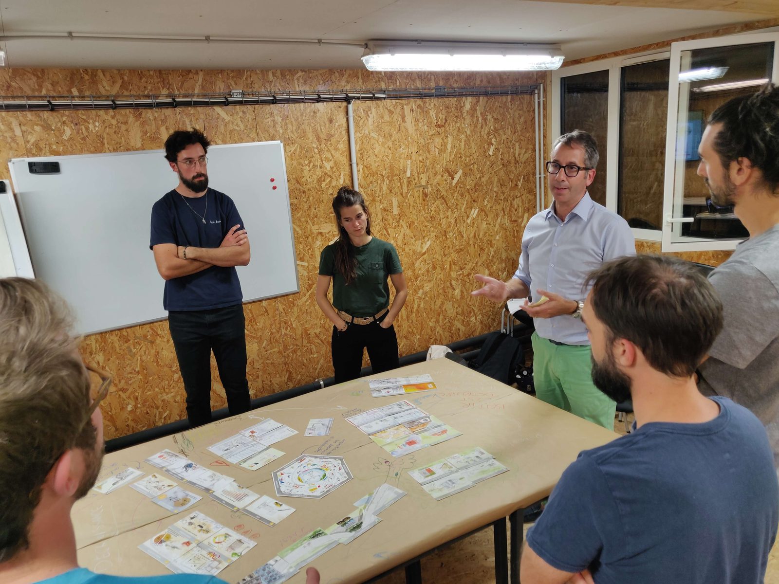 Atelier Fresque de la Construction : participants autour des cartes reliées sur une grande table, l'animateur échange avec le groupe