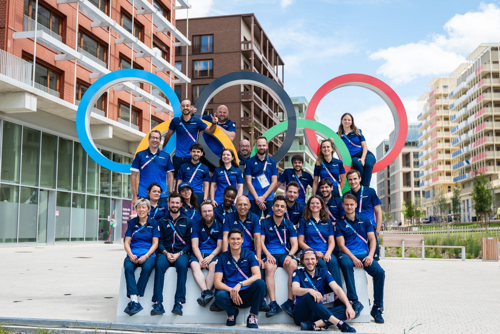 Équipe du Village olympique et paralympique Paris 2024 L'équipe facilités du village olympique en tenue Paris 2024, réunie devant les anneaux olympiques